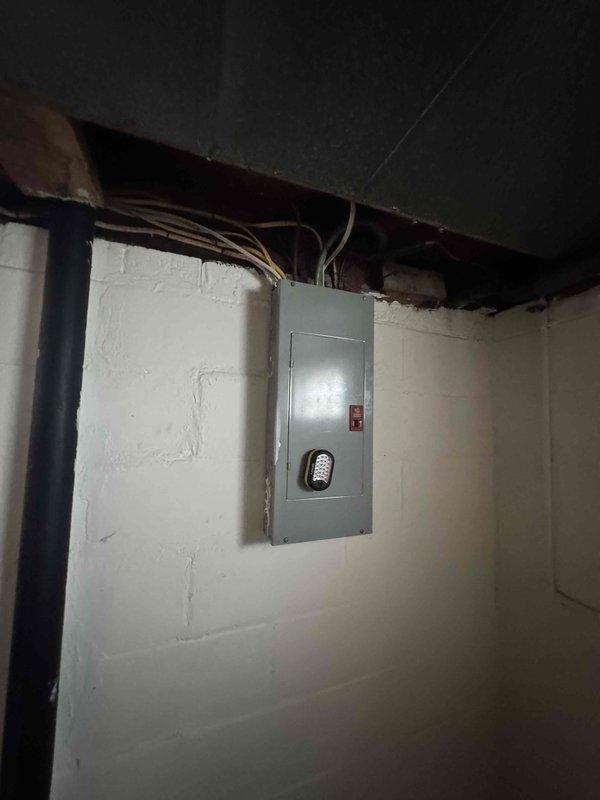 Conducted on-site evaluation for furnace replacement at residential property with 40-year-old non-operational heating system. Inspected existing cream-colored furnace unit with gray upper section located in basement utility area, noting complete system failure and age-related deterioration. Assessed existing ductwork configuration including flexible metallic ducts and rigid metal components connected to ceiling joists. Evaluated electrical infrastructure including main panel box and wiring capacity for new equipment installation. Documented basement mechanical room conditions, concrete block wall structure, floor joists, and available clearances for replacement unit. Provided comprehensive replacement estimate for new furnace system to restore heating functionality.