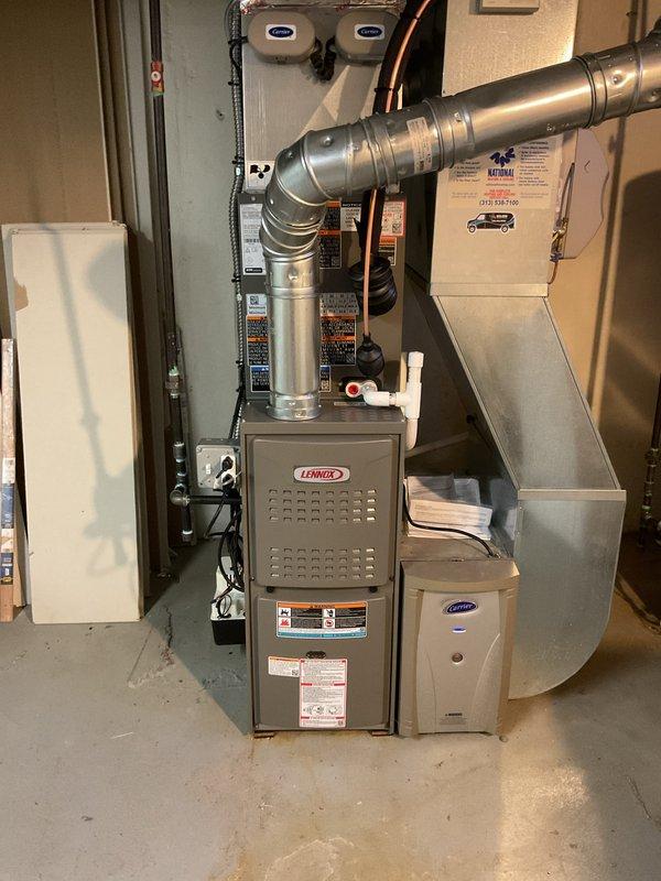 Completed full HVAC system installation including a Lennox 70,000 BTU furnace (model ML180UH070E36AK) and 2-ton air conditioning unit with rear discharge configuration. Installed all necessary ductwork with metallic silver curved supply runs extending from furnace cabinet, routed copper refrigerant lines along wall, and integrated Carrier auxiliary equipment into the system. Secured all mechanical and electrical connections, reconnected existing components to new system, and completed installation per permit requirements for mechanical and electrical work.