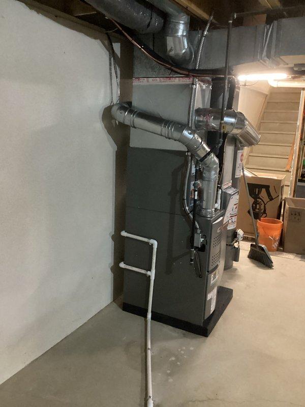 Completed full HVAC system installation in basement mechanical room, including 70,000 BTU furnace with rear-positioned 2-ton air conditioning unit. Installed complete ductwork assembly with rigid metallic and flexible aluminum ducting connected to ceiling joists, along with white PVC venting and drainage system. Reconnected humidifier to new furnace system and completed all electrical connections. All equipment mounted on proper platforms against concrete wall with appropriate clearances maintained for service access and code compliance.