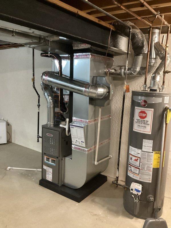Completed full HVAC system installation in basement mechanical room, including 70,000 BTU furnace with rear-positioned 2-ton air conditioning unit. Installed complete ductwork assembly with rigid metallic and flexible aluminum ducting connected to ceiling joists, along with white PVC venting and drainage system. Reconnected humidifier to new furnace system and completed all electrical connections. All equipment mounted on proper platforms against concrete wall with appropriate clearances maintained for service access and code compliance.