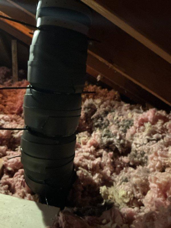 Responded to callback for post-installation issues on 110,000 BTU furnace and 4-ton AC system. Accessed attic space to inspect exhaust vent pipe reported as crooked and potentially unstable on roof penetration. Upon inspection, found flexible exhaust duct secured with metallic foil tape running vertically through attic insulation to roof exit point. Assessed structural integrity and mounting of exhaust termination. Additionally investigated booster fan malfunction reported as continuously running since original installation. Documented attic conditions showing loose-fill fiberglass insulation and ductwork routing for warranty and quality assurance purposes.