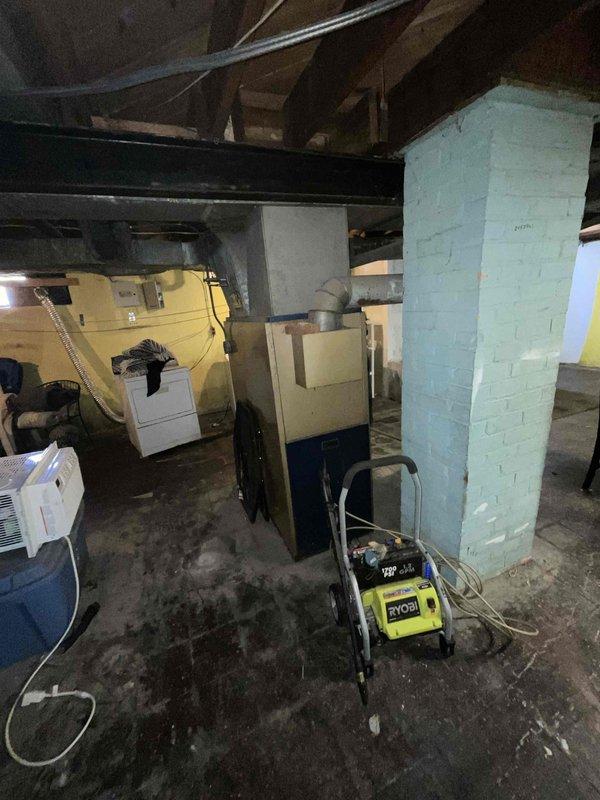 Conducted comprehensive site assessment for full HVAC system replacement in residential basement location. Evaluated existing dark-colored furnace unit and identified need for complete system upgrade including new furnace installation and addition of air conditioning system. Documented current equipment configuration, ductwork layout, electrical connections, and spatial requirements for proposed equipment installation. Assessed structural considerations including support columns, ceiling clearances, and access points for optimal system placement. Photographed existing HVAC components, water heater proximity, and available workspace to develop accurate replacement proposal meeting immediate timeline requirements for system upgrade within coming weeks.