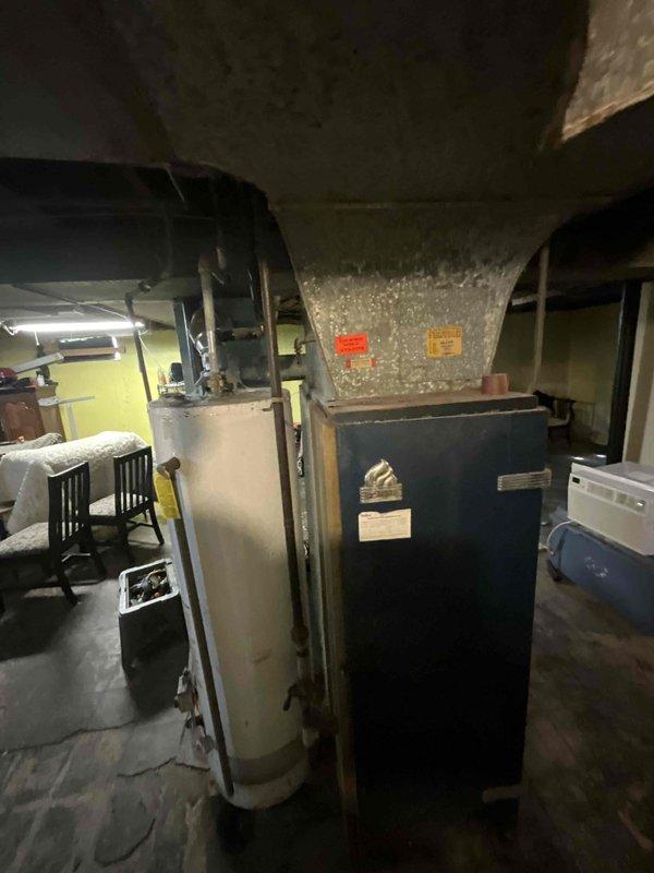 Conducted comprehensive site assessment for full HVAC system replacement in residential basement location. Evaluated existing dark-colored furnace unit and identified need for complete system upgrade including new furnace installation and addition of air conditioning system. Documented current equipment configuration, ductwork layout, electrical connections, and spatial requirements for proposed equipment installation. Assessed structural considerations including support columns, ceiling clearances, and access points for optimal system placement. Photographed existing HVAC components, water heater proximity, and available workspace to develop accurate replacement proposal meeting immediate timeline requirements for system upgrade within coming weeks.