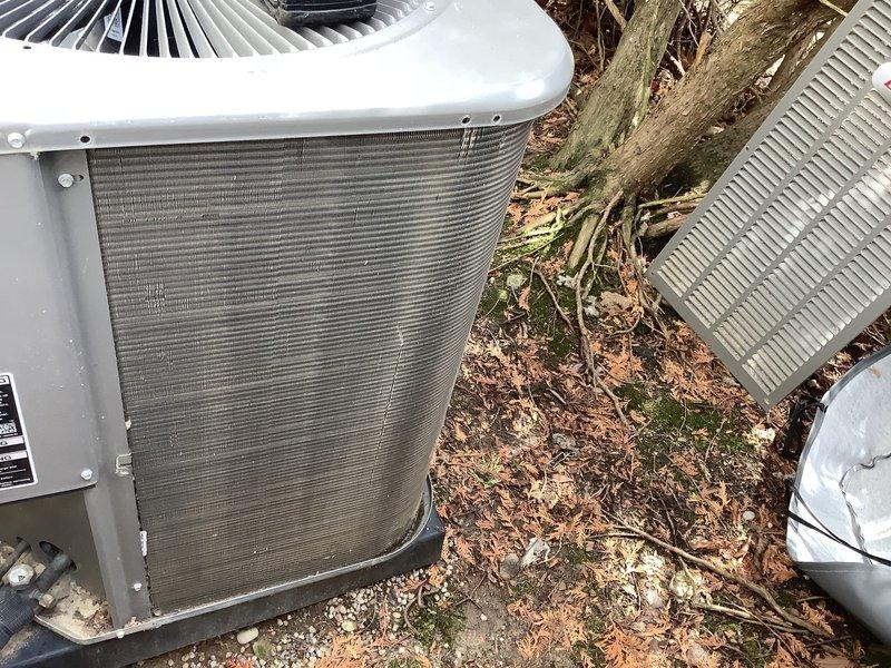 Completed final ComfortGuard maintenance visit on dual outdoor AC condenser units. Performed comprehensive inspection of both condensing units, including evaluation of cooling fins which showed accumulation of dirt and debris, checked fan guards, assessed electrical connections, and verified proper operation of all components. Documented equipment condition with photographs showing units positioned on concrete pad with natural debris accumulation from surrounding vegetation and tree roots, confirming maintenance completion for this recurring service agreement.