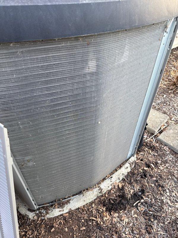 Completed annual cooling maintenance on outdoor condensing unit. Inspected condenser coil and fins, noting accumulation of dirt, debris, and organic matter on heat exchanger surfaces. Replaced air filter and evaporator pad as needed. Documented equipment condition with photos showing weathering and outdoor contamination on finned coil surfaces and cabinet exterior.