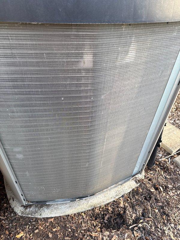 Completed annual cooling maintenance on outdoor condensing unit. Inspected condenser coil and fins, noting accumulation of dirt, debris, and organic matter on heat exchanger surfaces. Replaced air filter and evaporator pad as needed. Documented equipment condition with photos showing weathering and outdoor contamination on finned coil surfaces and cabinet exterior.