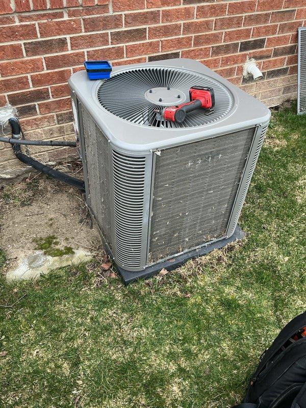 Completed routine air conditioning maintenance on residential outdoor condenser unit. Performed comprehensive AC tune-up including visual inspection of unit exterior, cabinet, and fan grille assembly. Connected manifold gauges to service ports and verified refrigerant pressures and system charge levels. Inspected electrical disconnect, conduit connections, and refrigerant line sets along brick wall mounting. Evaluated condenser coil condition through louvers, noting normal outdoor weathering and minor surface accumulation. Confirmed fan motor operation and proper airflow through top-mounted grille. Tested system performance and verified unit operating within manufacturer specifications. All components functioning properly with no deficiencies noted requiring immediate attention.