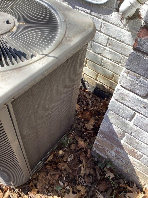 Completed comprehensive ComfortGuard maintenance package on outdoor HVAC condenser unit. Cleared significant accumulation of dried leaves and organic debris from around unit and confined space between equipment and building wall to restore proper airflow and prevent potential system efficiency issues. Performed standard maintenance inspection and service procedures on the air conditioning system.
