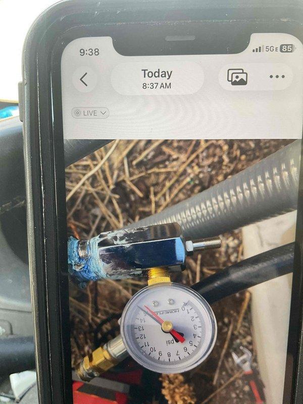 Performed pressure test on HVAC system using calibrated gauge equipment with brass fittings and blue valve assembly. Test conducted on outdoor unit to verify system integrity, with pressure readings monitored and documented via gauge positioned at ground level near flexible metallic conduits and refrigerant lines. All connections secured and system confirmed operational within manufacturer specifications.
