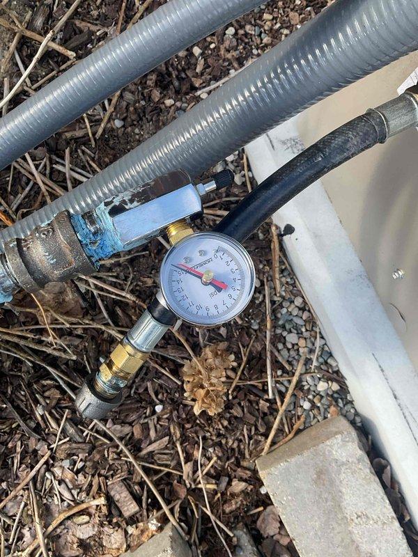 Performed pressure test on HVAC system using calibrated gauge equipment with brass fittings and blue valve assembly. Test conducted on outdoor unit to verify system integrity, with pressure readings monitored and documented via gauge positioned at ground level near flexible metallic conduits and refrigerant lines. All connections secured and system confirmed operational within manufacturer specifications.