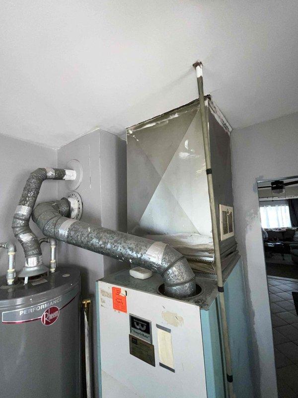 Conducted on-site assessment for complete HVAC system replacement in residential property. Evaluated existing aging furnace unit located in interior utility closet, which was determined to be incompatible with central air conditioning integration due to system age and design limitations. Documented current equipment configuration including vertical air handler setup with adjacent water heater installation and existing ductwork routing. Photographed mechanical room layout, equipment specifications, and spatial constraints to prepare comprehensive replacement estimate for new furnace and central air conditioning system installation.