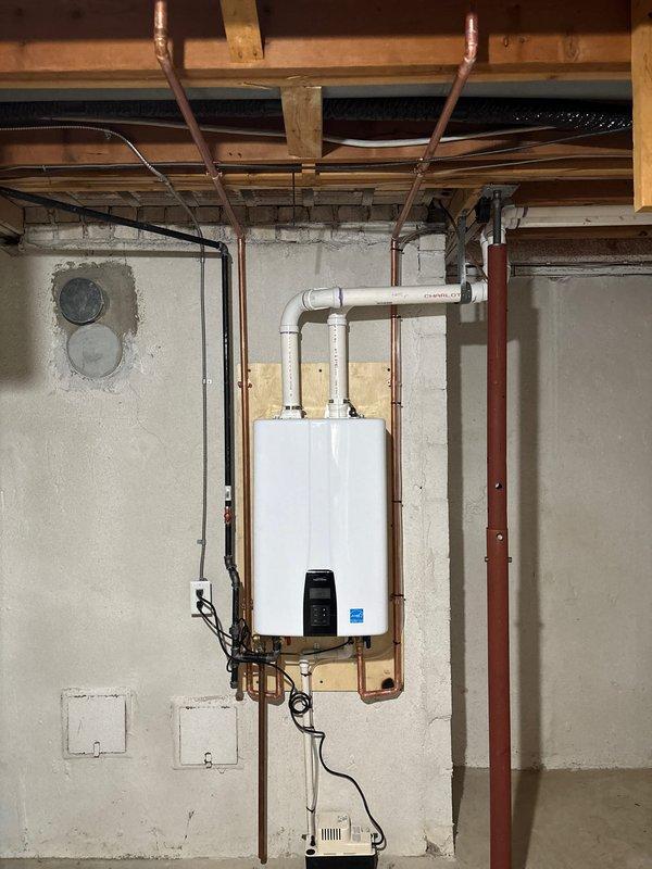 Completed full installation of Energy Star certified tankless water heater in basement mechanical room, mounted to concrete block wall with proper structural support. Installed new copper supply piping with inverted U-configuration, routed black electrical conduit and wiring for dedicated circuit, and connected white PVC exhaust/intake venting system through exterior brick wall with appropriate termination fittings and mounting brackets. All mechanical and electrical permits obtained prior to installation, ensuring code-compliant setup with organized pipe routing and professional finish.