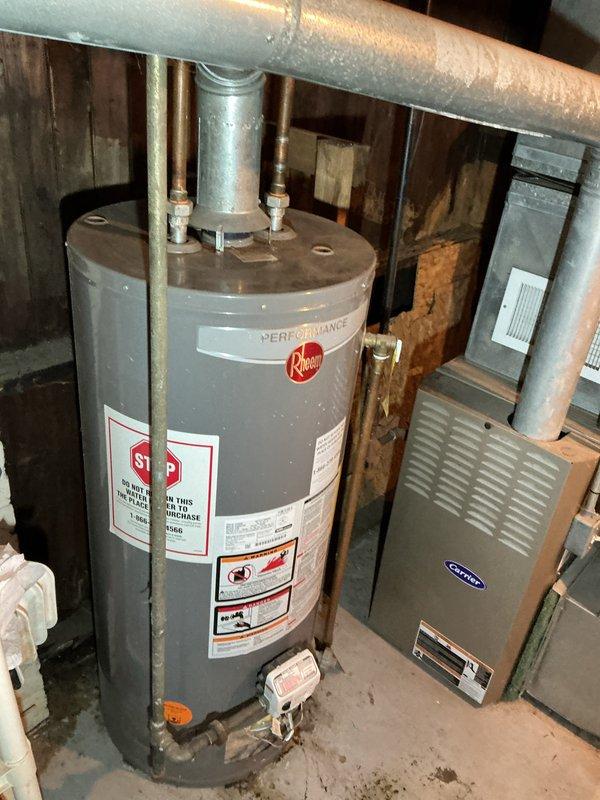 Responded to hot water issue affecting specific area of 115-year-old residence, ongoing for two weeks. Inspected 10-year-old Rheem tanked water heater in basement utility area. Evaluated unit connections, gas valve operation, and plumbing distribution system. Observed evidence of previous moisture issues on concrete floor surrounding water heater base. Assessed unit performance, verified proper gas supply, and examined hot water distribution piping to affected zones. Documented water heater condition and surrounding mechanical systems including adjacent HVAC equipment. Provided assessment findings and recommendations to homeowner.