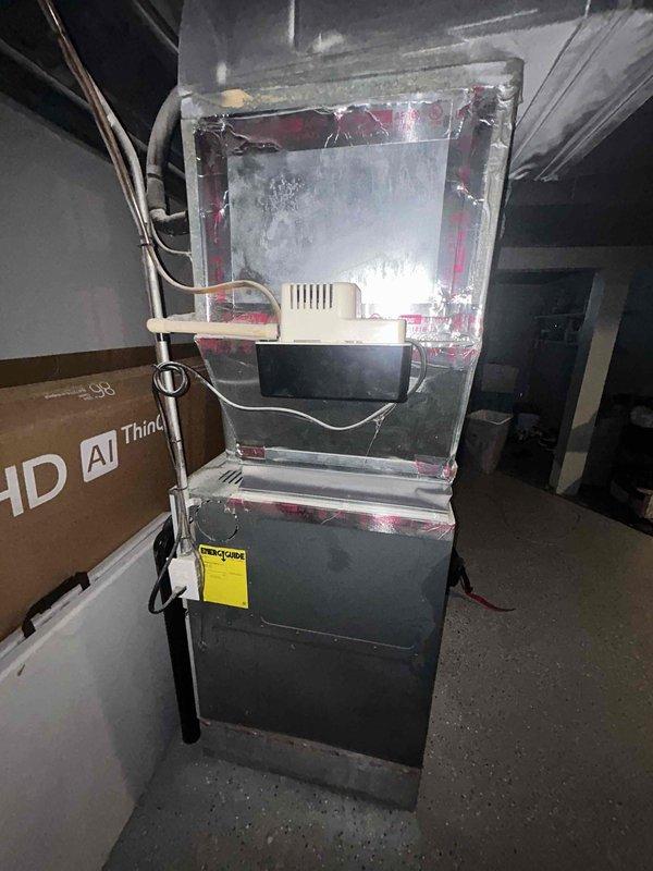 Responded to assess storm-damaged AC condensing unit in basement after tree branch impact. Found older high-efficiency Rheem unit rotated approximately 30 degrees from original installation position with compromised structural integrity. Documented extensive damage including bent hail guard frame, torn fan mounting strut support, and one completely cracked/broken fan mounting strut. Determined refrigerant brazing lines have been compromised due to forced angular displacement, creating safety concerns and potential for refrigerant leaks with further movement. Fan assembly deemed unsafe for operation due to damaged mounting frame presenting risk of catastrophic motor and blade failure. Recommended safe refrigerant recovery prior to any further disturbance and advised against repair attempts due to extent of structural damage. Provided estimate for complete system replacement.