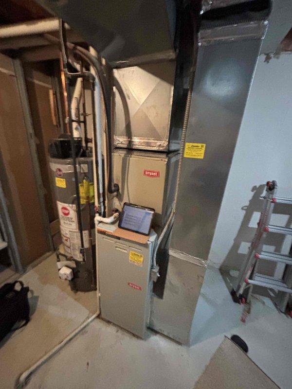 Conducted on-site assessment for furnace replacement estimate on 25-year-old Bryant heating system located in basement mechanical room. Inspected existing furnace installation, ductwork connections, and associated components including water heater proximity and available workspace. Documented current equipment condition showing aged furnace with standard vertical installation, proper ductwork routing, and existing PVC drain lines. Evaluated exterior air conditioning condenser unit on concrete pad to assess compatibility for potential system replacement options. Photographed mechanical room layout, equipment specifications, clearances, and utility connections to prepare comprehensive replacement quote. Confirmed basement access for equipment removal and new installation, noting concrete floor and adequate working space. Assessed electrical service, gas line connections, and existing vent configuration for replacement system requirements.
