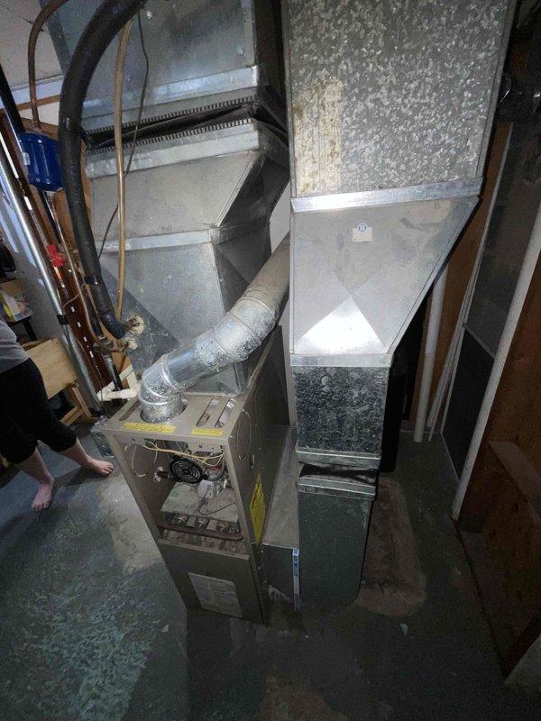 Conducted on-site assessment and provided replacement estimate for 27-year-old furnace and air conditioning system. Documented existing HVAC equipment condition, including basement-installed upright furnace with metal ductwork and plenum assembly, noting significant water accumulation on concrete floor surrounding unit base indicating potential condensate drain failure or leak. Photographed current system configuration and presented replacement options for complete heating and cooling system upgrade.