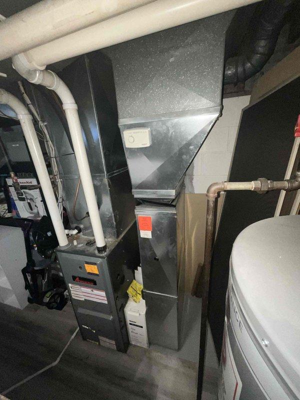 Conducted comprehensive assessment of existing 15-year-old HVAC system including furnace and air conditioning unit for replacement estimate. Documented current equipment configuration in basement mechanical room, noting gray metal furnace with PVC venting system and adjacent air handler unit. Evaluated system layout, existing ductwork connections, black flexible duct routing, and copper piping infrastructure. Photographed all equipment specifications, manufacturer labels, and mechanical components to prepare detailed replacement quote for complete furnace and AC installation.