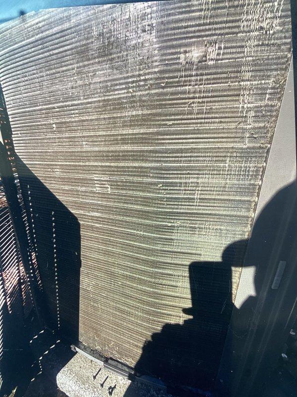 Performed scheduled ACM maintenance on rooftop HVAC unit. Inspected cylindrical condenser coil assembly and documented significant accumulation of dust, dirt, and debris on aluminum fin surfaces causing airflow restriction. Noted visible streaking, staining patterns, and mineral deposits across metallic fins indicating weathering and outdoor exposure requiring cleaning to restore optimal system performance.