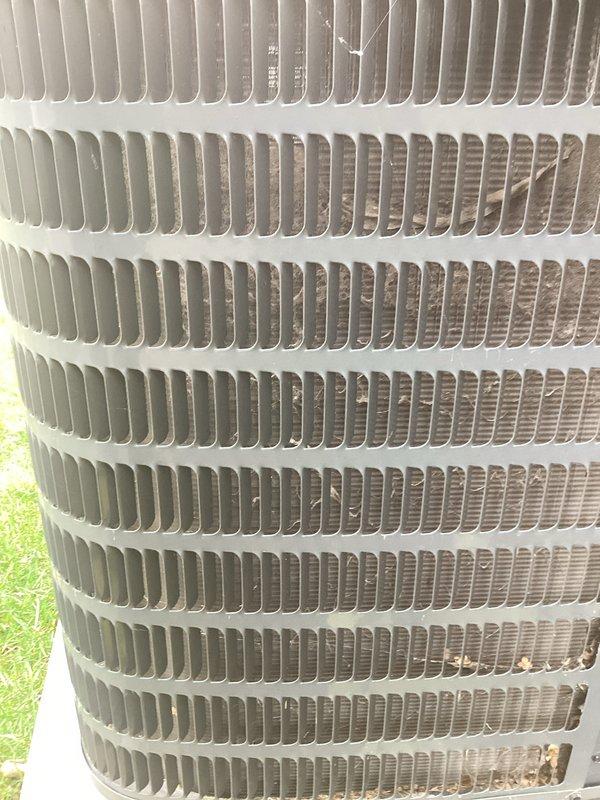 Completed annual maintenance on outdoor air conditioning condenser unit. Performed comprehensive inspection of heat exchanger coil fins, noting light to moderate dirt accumulation and discoloration on lower sections with minor debris caught in upper fin rows. Cleared organic debris including leaves and twigs from around unit base and concrete pad. Verified condenser positioning on concrete foundation and checked overall system condition. Unit fins showed normal weathering consistent with outdoor exposure, with uniform spacing maintained throughout coil assembly.
