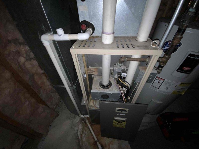 Conducted on-site assessment for complete HVAC system replacement in above-ground basement location. Existing 20-year-old natural gas furnace and air conditioning system were non-operational and required full replacement. Evaluated current equipment configuration including gas furnace unit, associated PVC condensate drainage system, refrigerant line sets, electrical connections, and ductwork installation within exposed basement utility area. Documented existing system layout with furnace positioned on concrete floor with wooden platform support structure, multiple PVC drain lines, copper refrigerant tubing, gas valve assembly, and integration with water heating equipment. Assessed installation environment including foundation walls, exposed ceiling joists, existing ductwork routing, and available space for new equipment placement. Provided comprehensive replacement estimate for new high-efficiency air conditioning and natural gas furnace system to restore climate control functionality.