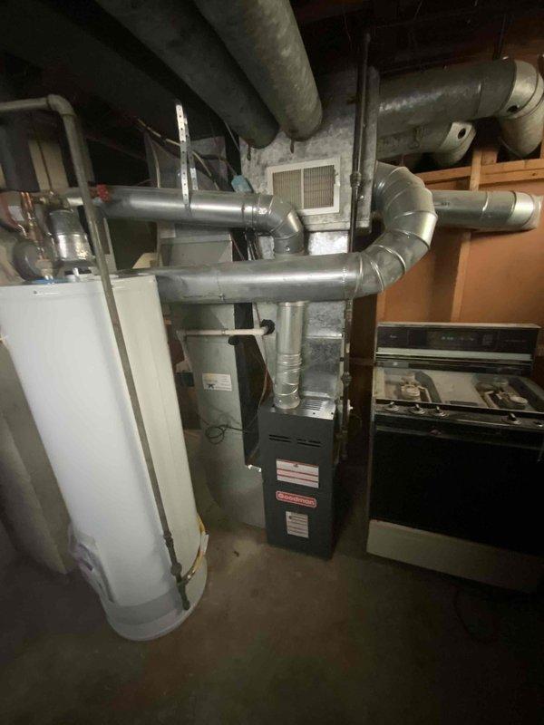 Provided estimate for complete HVAC system replacement in basement location, including furnace and air conditioning unit under BOGO promotion. Existing 15-year-old furnace currently operational but nearing end of service life, with air conditioning system exceeding 30 years and requiring replacement. Equipment located in unfinished basement mechanical room with concrete floor, exposed ceiling joists, and existing ductwork infrastructure in place.