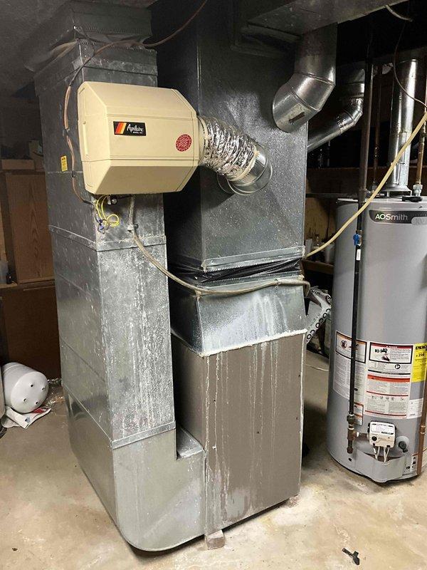 Conducted estimate for complete air conditioning system replacement. Existing outdoor condenser unit is approximately 30 years old, dating back to 1990s installation, showing significant age-related wear and deterioration. Indoor furnace system with attached humidifier located in basement utility area exhibits moisture damage evidenced by white mineral deposits and efflorescence streaking down unit sides. Evaluated current system configuration including ductwork connections, electrical service, and equipment placement. Documented equipment conditions through photographic assessment of both indoor and outdoor components. Provided recommendations for new AC system installation to replace aging equipment that has exceeded typical service life expectancy.
