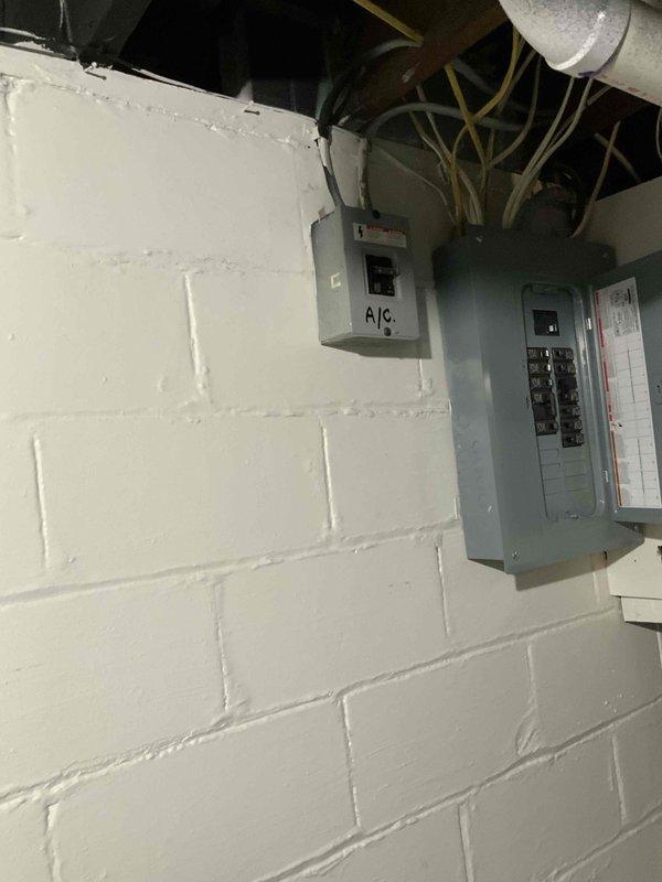 Conducted site evaluation for new air conditioning system installation at residential single family home with no existing AC unit. Assessed electrical infrastructure in basement utility area, documenting existing electrical panels and circuit breaker capacity to determine compatibility and requirements for new AC system installation. Photographed electrical service panels, conduit routing, and available space for future equipment connections to support accurate equipment sizing and installation planning.