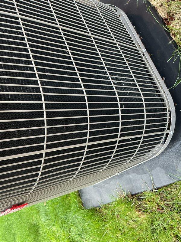 Performed scheduled maintenance on residential outdoor air conditioning condenser unit. Inspected top protective grille, condenser coils, and fan assembly for proper operation and debris accumulation. Unit showed normal weathering consistent with outdoor exposure, with dirt and organic debris present on grille surface and surrounding concrete pad. Verified equipment operational status and documented current condition of condenser casing, protective components, and installation pad for maintenance records.