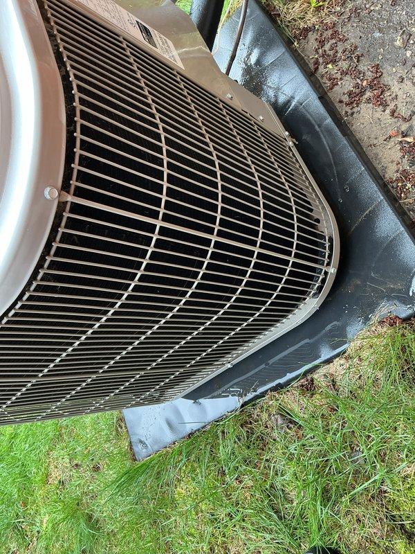 Performed scheduled maintenance on residential outdoor air conditioning condenser unit. Inspected top protective grille, condenser coils, and fan assembly for proper operation and debris accumulation. Unit showed normal weathering consistent with outdoor exposure, with dirt and organic debris present on grille surface and surrounding concrete pad. Verified equipment operational status and documented current condition of condenser casing, protective components, and installation pad for maintenance records.