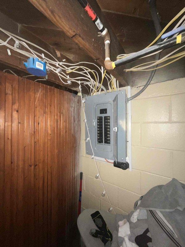 Conducted on-site assessment for complete air conditioning system replacement. Evaluated existing electrical infrastructure in basement utility area, documenting current electrical panel configuration and available circuit capacity to determine compatibility requirements for new AC installation. Photographed electrical service panel showing dual-row circuit breaker arrangement with multiple branch circuits, noting wire routing from panel to ceiling joists and overall electrical system condition. Assessed basement space layout including exposed ceiling joists, concrete block walls, and available pathways for new refrigerant lines and electrical connections. Documented unfinished basement conditions to plan equipment placement, condensate drainage routing, and necessary modifications to support new system installation. Evaluation complete; prepared comprehensive estimate for customer review including equipment specifications and installation requirements.