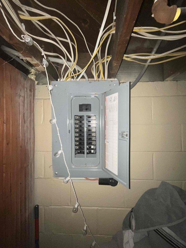 Conducted on-site assessment for complete air conditioning system replacement. Evaluated existing electrical infrastructure in basement utility area, documenting current electrical panel configuration and available circuit capacity to determine compatibility requirements for new AC installation. Photographed electrical service panel showing dual-row circuit breaker arrangement with multiple branch circuits, noting wire routing from panel to ceiling joists and overall electrical system condition. Assessed basement space layout including exposed ceiling joists, concrete block walls, and available pathways for new refrigerant lines and electrical connections. Documented unfinished basement conditions to plan equipment placement, condensate drainage routing, and necessary modifications to support new system installation. Evaluation complete; prepared comprehensive estimate for customer review including equipment specifications and installation requirements.