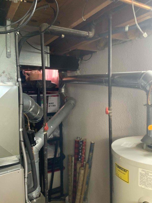 Conducted on-site assessment and documentation of existing residential water heater installation in utility room. Photographed current white cylindrical water heater unit with all associated plumbing connections, including copper supply lines, brass valves, gray PVC piping, and safety components. Documented equipment condition, surrounding mechanical systems, and installation configuration to provide comprehensive estimate for water heater replacement.