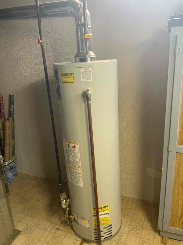 Conducted on-site assessment and documentation of existing residential water heater installation in utility room. Photographed current white cylindrical water heater unit with all associated plumbing connections, including copper supply lines, brass valves, gray PVC piping, and safety components. Documented equipment condition, surrounding mechanical systems, and installation configuration to provide comprehensive estimate for water heater replacement.