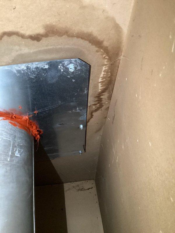 Responded to service call for furnace leaking water in closet location. Upon inspection, discovered significant water damage and staining around flue pipe penetration through ceiling, indicating condensate leak from high-efficiency furnace exhaust system. Identified improper sealing and potential blockage in condensate drainage system causing water to back up and leak around vent pipe assembly. Documented existing water damage to drywall and ceiling materials surrounding the metal flue pipe and mounting flange. Equipment is under both parts and labor warranty coverage.