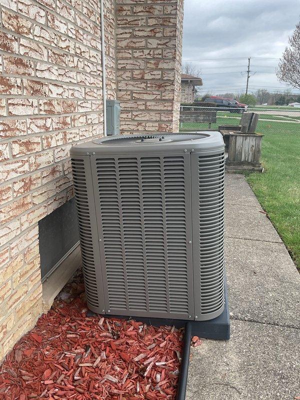 Completed annual cooling maintenance on residential outdoor AC unit. Brought and installed new filter and evaporator pad as scheduled. Inspected condenser unit positioned on concrete pad against exterior wall, verified proper operation of fan assembly and louvers, and documented equipment condition with photos showing unit in serviceable state with adequate clearance from surrounding mulch bed.