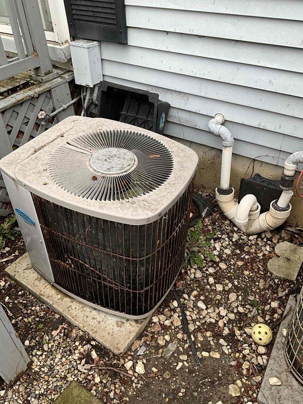 Conducted on-site evaluation for complete HVAC system replacement in residential side-by-side condo unit. Assessed existing olive-green furnace located in basement mechanical room with connected ductwork assembly showing age-related wear and surface discoloration. Evaluated outdoor condensing unit positioned on concrete pad against exterior wall, noting weathered white/beige cabinet with circular top-discharge fan grille, flexible conduit electrical connection, and proximity to PVC plumbing configuration. Documented current equipment conditions through photographic inspection to provide comprehensive replacement estimate for furnace and air conditioning system planned for installation within upcoming two-week timeframe.