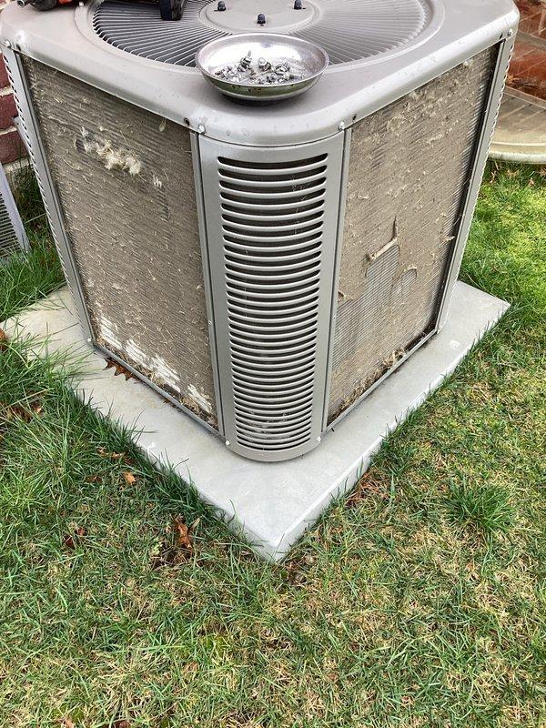 Completed annual cooling maintenance on residential split system air conditioning unit. Performed comprehensive inspection of outdoor condenser unit, noting heavy exterior soil and grime accumulation on cabinet panels requiring cleaning. Removed fan grille to access internal components, inspected condenser coils through protective mesh panels, verified refrigerant line connections at wall penetration, checked mounting and pad stability, and documented equipment condition. Unit operational with all safety features intact upon completion of preventive maintenance service.