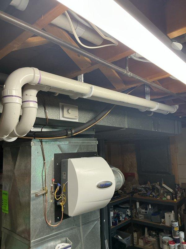 Completed full HVAC system installation including a 90,000 BTU gas furnace and 3-ton air conditioning unit with rear discharge configuration. Installed condensate drainage system with white PVC piping routed along exterior foundation wall, mounted outdoor condenser unit on gravel pad adjacent to building foundation, and completed all refrigerant line connections. Added whole-home humidifier unit to furnace ductwork in basement mechanical room with proper water supply and drainage connections, secured all copper refrigerant lines to ceiling joists, and reconnected all electrical components to existing service. Mechanical and electrical permits were obtained prior to installation, and all work was completed per code requirements with system tested and operational upon completion.