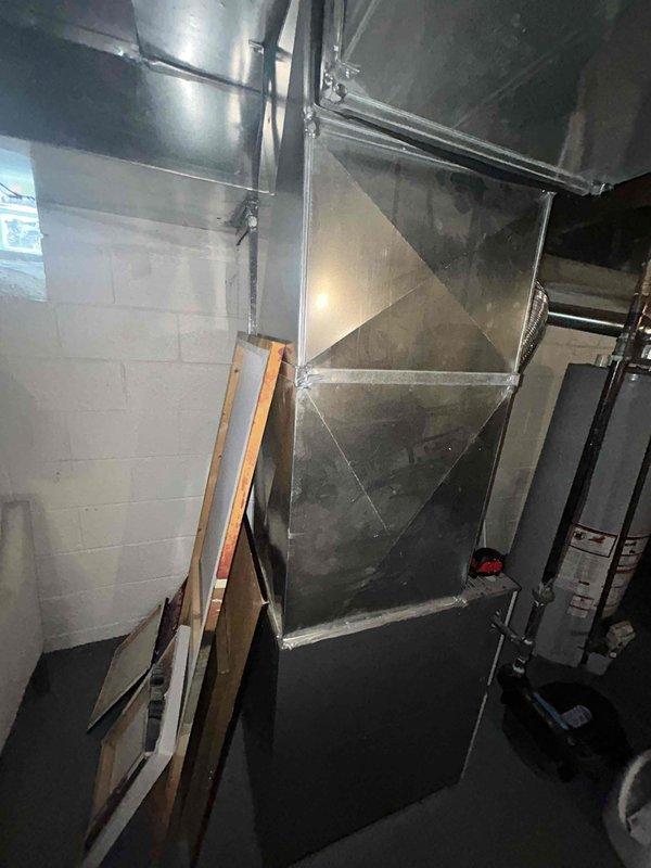 Conducted on-site evaluation for HVAC equipment replacement estimate in residential property. Assessed existing furnace installation located in basement utility area with current ductwork configuration including metallic flex ducting and sheet metal plenum system. Documented equipment layout, ductwork connections, and spatial requirements for potential air conditioning system installation and possible furnace replacement. Photographed existing HVAC infrastructure to support equipment sizing recommendations and installation planning.