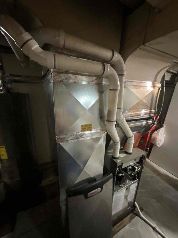 Conducted comprehensive assessment of non-functional residential air conditioning system in basement utility area alongside existing 5-year-old natural gas furnace. Documented current HVAC configuration including furnace unit with diamond-pattern casing, existing PVC condensate drainage network, and measured clearance dimensions of 20.5 inches and 23 inches for equipment replacement planning. Evaluated installation space constraints with adjacent water heater and water treatment equipment to determine optimal positioning for new air conditioning system compatible with existing natural gas heating infrastructure.