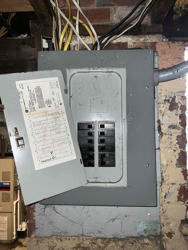 Completed full HVAC system estimate for outdoor air conditioning installation at commercial brick building location. Documentation included exterior condenser unit positioning on gravel pad with proper clearances, electrical metering infrastructure with three-meter assembly, dedicated disconnect box installation, and conduit routing along exterior wall. Interior electrical panel assessment showed dual-column breaker configuration with multiple feed cables entering from above, supporting system power requirements for complete HVAC installation.