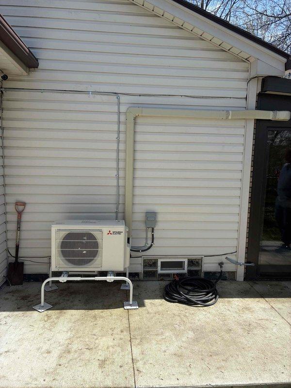 Completed installation of Mitsubishi Electric mini-split system at residential property. Installed outdoor condensing unit on white metal mounting bracket with concrete pad placement, ran refrigerant line set and electrical conduit vertically along exterior siding to wall penetration, and mounted indoor head unit on interior brick wall of covered patio area. New electrical circuit installed with disconnect box, mechanical and electrical permits obtained, and all paperwork finalized with signed financing documents and identification on file.