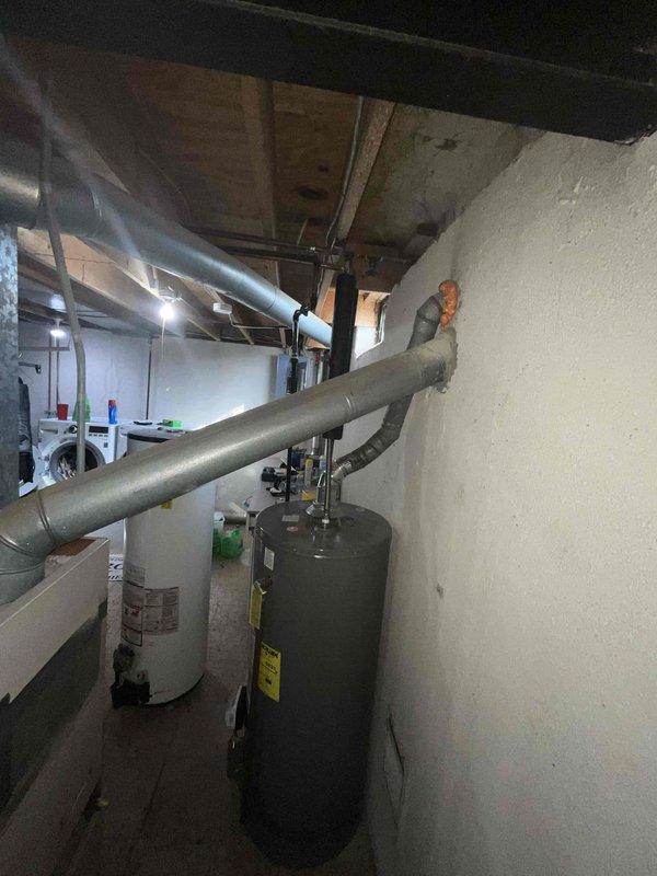 Conducted comprehensive site evaluation for complete HVAC system replacement at residential property. Existing 16-year-old air conditioning unit experiencing failure, blowing hot air instead of cooling. Assessed basement mechanical room containing aging furnace with two-tone exterior casing and cylindrical water heater. Documented existing ductwork configuration including large galvanized metal supply and return ducts running horizontally across exposed ceiling joists. Evaluated current system layout, clearances, and installation access points for full system replacement. Photographed equipment positioning, duct connections, electrical service, and mechanical room infrastructure to prepare detailed replacement proposal. Provided comprehensive estimate for new HVAC system installation to address immediate cooling failure and aging equipment concerns.