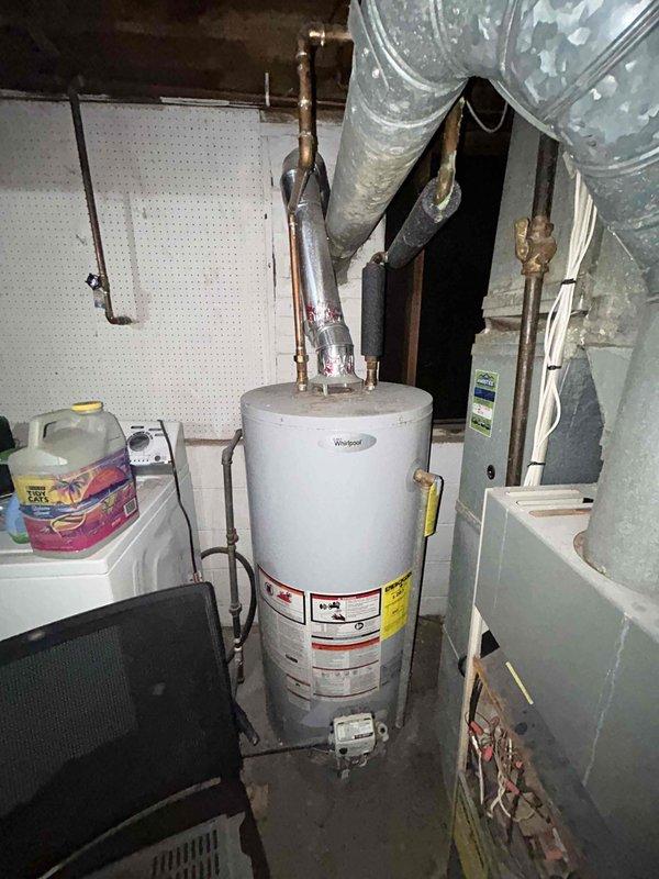 Conducted comprehensive HVAC system evaluation for furnace and air conditioning replacement estimate at lower tri-level residence with 18-year-old existing natural gas heating and cooling equipment currently in operational condition. Assessed existing furnace unit located in basement mechanical room, documenting current system configuration including ductwork layout, venting arrangements, and electrical connections. Evaluated air conditioning system components and refrigerant line routing. Photographed existing HVAC installation showing furnace cabinet with control panels, extensive galvanized ductwork with age-related dust accumulation, copper piping throughout mechanical space, and overall equipment positioning relative to water heater and available workspace. Documented white cinder block wall construction, exposed floor joists, concrete flooring, and utility room access considerations for future equipment replacement planning.