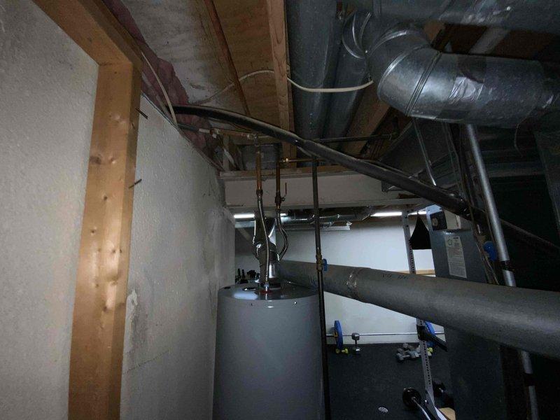 Completed full system HVAC estimate for a mid-large residential property (2000-3000 sq.ft.) requiring heating and cooling equipment installation in basement location. Assessment included existing mechanical infrastructure with water heater, plumbing lines, ductwork configuration, and central humidifier system to determine specifications for natural gas or propane-fueled furnace and air conditioning unit replacement. Documented current system layout including galvanized metal ductwork, air handler plenum, exposed piping with shut-off valves, and structural considerations for new equipment placement within unfinished utility space.
