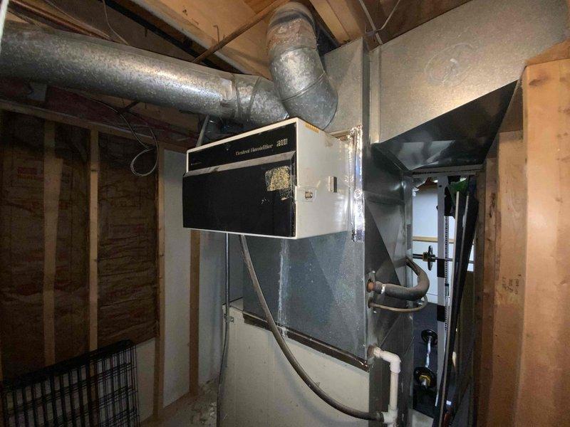 Completed full system HVAC estimate for a mid-large residential property (2000-3000 sq.ft.) requiring heating and cooling equipment installation in basement location. Assessment included existing mechanical infrastructure with water heater, plumbing lines, ductwork configuration, and central humidifier system to determine specifications for natural gas or propane-fueled furnace and air conditioning unit replacement. Documented current system layout including galvanized metal ductwork, air handler plenum, exposed piping with shut-off valves, and structural considerations for new equipment placement within unfinished utility space.