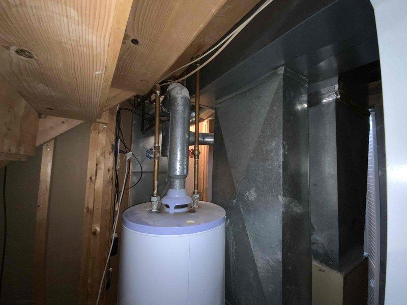 Provided comprehensive replacement estimate for 25-year-old residential HVAC system located in basement utility area. Assessed existing furnace, air conditioning unit, and hot water heater for complete system replacement, with current furnace being the only operational component. Documented existing equipment configuration including dark gray heating/cooling unit, cylindrical water heater with expansion tank and copper piping, and associated ductwork within confined mechanical room space accessed through louvered bifold doors.
