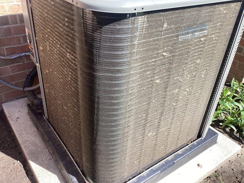 # HVAC Maintenance - Air Conditioning Unit

Performed routine preventative maintenance on residential outdoor condensing unit as part of recurring Air Care Cooling service agreement. Inspected heat pump system positioned on concrete pad adjacent to building exterior. Unit showed moderate accumulation of dirt, dust, and environmental debris on protective mesh grilles and heat exchanger coil fins, consistent with normal outdoor exposure.

Conducted comprehensive system evaluation including visual inspection of condenser coil condition, cabinet integrity, and drain pan assembly. Noted discoloration and particulate buildup on exterior surfaces and coil fins requiring attention. Assessed mounting hardware, protective housing, and base pan for proper positioning and structural integrity. Verified adequate clearance from surrounding vegetation and building structure for optimal airflow and system performance.

Cleaned condenser coils to remove accumulated dirt and debris from fin surfaces and