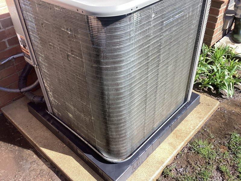# HVAC Maintenance - Air Conditioning Unit

Performed routine preventative maintenance on residential outdoor condensing unit as part of recurring Air Care Cooling service agreement. Inspected heat pump system positioned on concrete pad adjacent to building exterior. Unit showed moderate accumulation of dirt, dust, and environmental debris on protective mesh grilles and heat exchanger coil fins, consistent with normal outdoor exposure.

Conducted comprehensive system evaluation including visual inspection of condenser coil condition, cabinet integrity, and drain pan assembly. Noted discoloration and particulate buildup on exterior surfaces and coil fins requiring attention. Assessed mounting hardware, protective housing, and base pan for proper positioning and structural integrity. Verified adequate clearance from surrounding vegetation and building structure for optimal airflow and system performance.

Cleaned condenser coils to remove accumulated dirt and debris from fin surfaces and