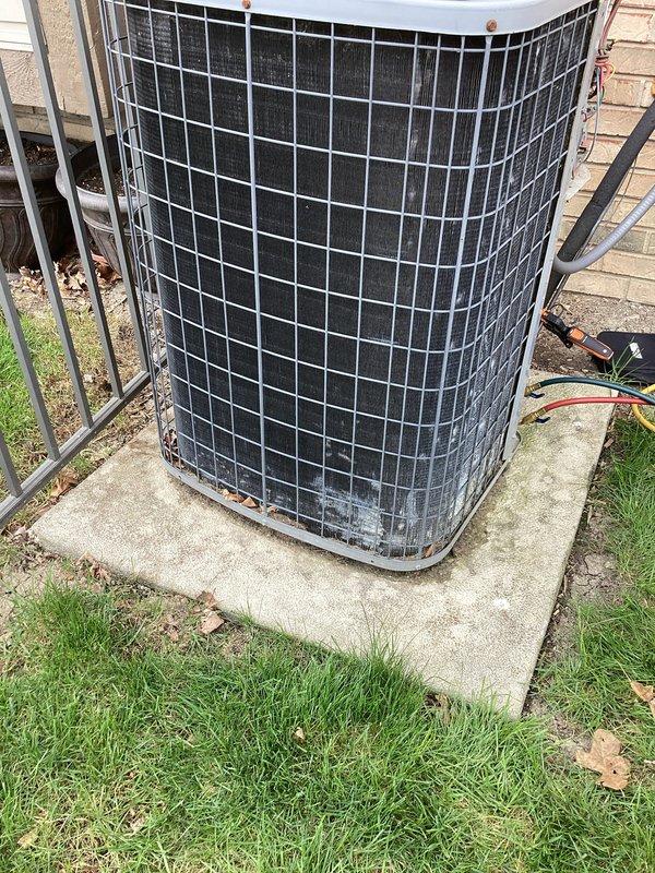 Completed scheduled maintenance on outdoor air conditioning condenser unit. Performed comprehensive inspection of cylindrical condenser system with protective wire guard cage, verified unit operational status, and documented equipment condition through photographic records. All components found functioning within normal parameters with unit showing typical age-related wear on exterior protective cage and minor base discoloration consistent with outdoor exposure.